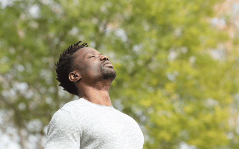 Homem na natureza olhando para o céu de olhos fechados.